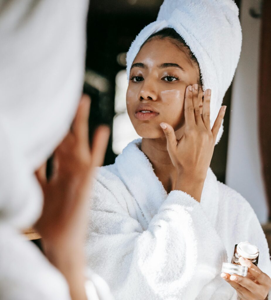 If You Want To Look Younger, Start Fixing These 15 Habits First woman applying moisturizer in mirror for glowing younger looking skin